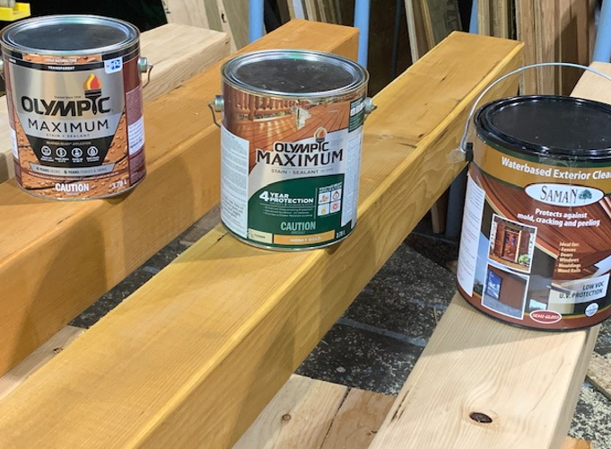 3 large cans of wood stain sitting on wooden timbers